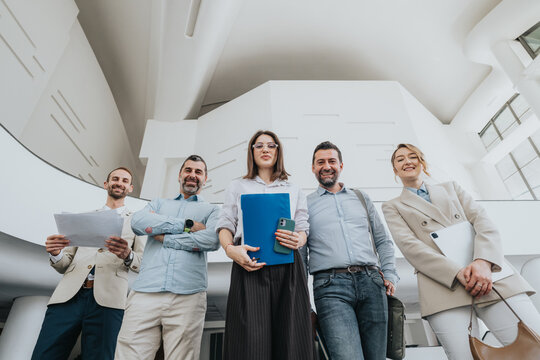 A diverse group of coworkers and friends stands together in a bright, modern office space. They hold documents and devices, conveying teamwork, confidence, and professional camaraderie.