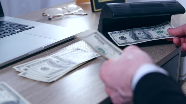 A man behind a chair checks money for authenticity or counterfeit under an ultraviolet lamp.