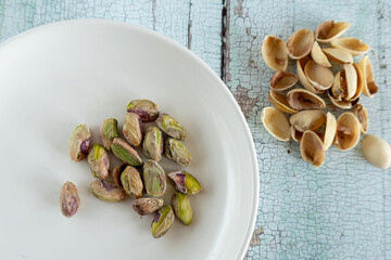 Shelled pistachios in white plate on rustic table with shells