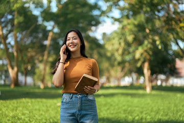Young Asian woman talking on phone while holding book