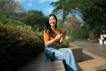Asian woman smiling while relaxing outdoors with smartphone