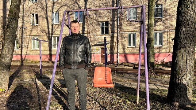Man standing near an empty swing set in a courtyard on a sunny autumn day - Powered by Adobe