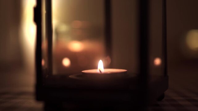 Lit candle in a lantern glowing warmly in a dark, cozy atmosphere.