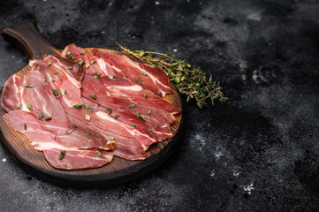 Slovenian ham, sliced cured pork meat on wooden board, Prsut. black background. top view