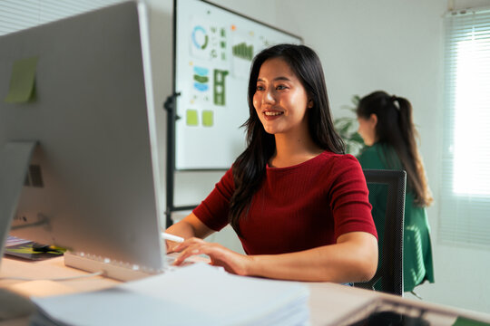 Asian businesswoman smiling while working with computer - Powered by Adobe