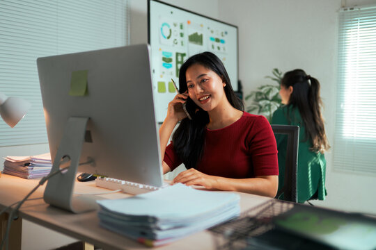 Asian businesswoman talking on phone at office desk