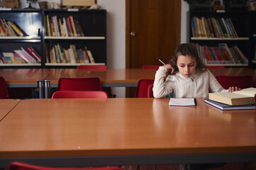 Young Girl Studying At Library Table With Books And Notepad