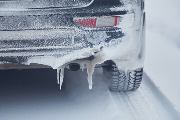 Icicles on the rear bumper of a car near the exhaust pipe in winter