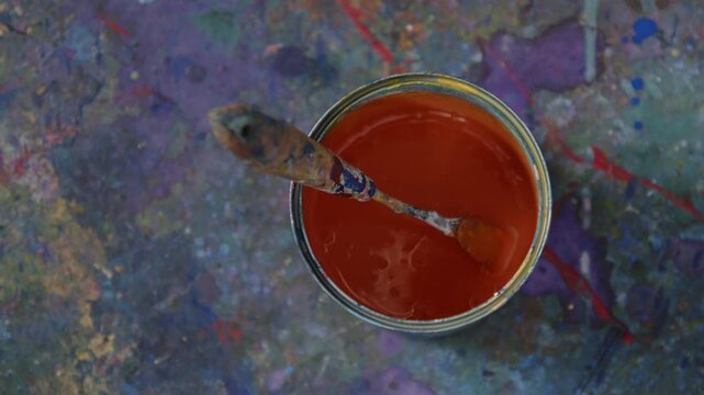 Spachtel liegt in orangefarbener Farbe im Eimer &ndash; ruhige Studioszene mit leichtem Zoom, kreativer Arbeitsumgebung und k&uuml;nstlerischem Malprozess