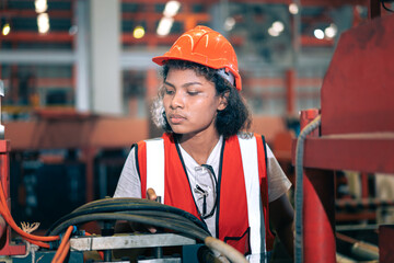 Professional Black African female factory engineer/worker/technician operate machinery in modern industrial plant. She wear safety helmet,vest show focus,skill in repair maintenance production process