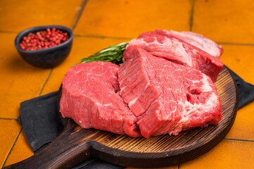 Raw beef fillet tender steaks on a decorative wooden board, fresh meat ready for grill. orange background. top view