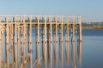 A wooden stilt pier reflected in the calm waters of the lake.