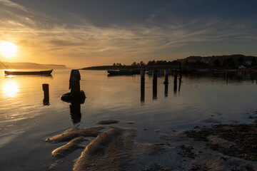 Sunset on a lagoon with silhouettes of boats and lampposts in the water. © ANTONIO