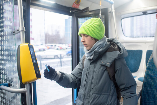 A teenage boy holds his card to a contactless payment terminal or validator. A child stands on a bus near the open doors in winter.