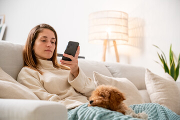 Woman relaxing at home checking smartphone with dog