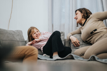 Obraz premium A joyful moment of familial bonding as a mother and daughter share laughter and lightheartedness on the couch in their cozy living room.