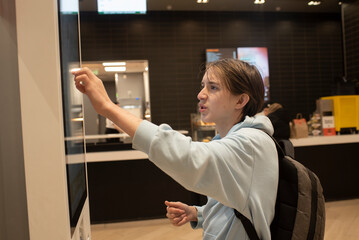 A teenage boy orders food from a self-service kiosk or terminal at a food court.