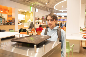 Teenage boy holding food tray, placing it on used tray table at food court.