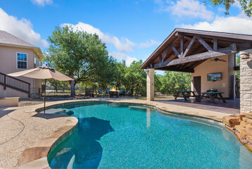 A large swimming pool in front of a house has several umbrellas