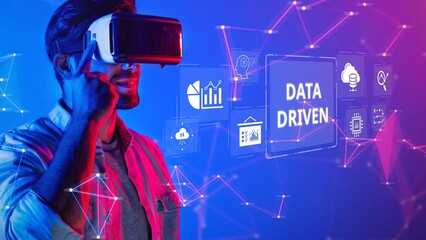 A young man uses a virtual reality headset to engage with colorful data visualizations, representing the intersection of technology and innovative information analysis. Raster