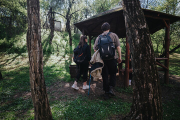 Hikers stand with backpacks near a rustic wooden shelter in dappled forest light, ready to continue their nature walk. The scene captures outdoor adventure, camaraderie, and exploration amid trees.
