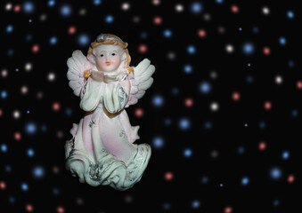 A little angel in pink clothes with wings on a black background with lights of different colors.