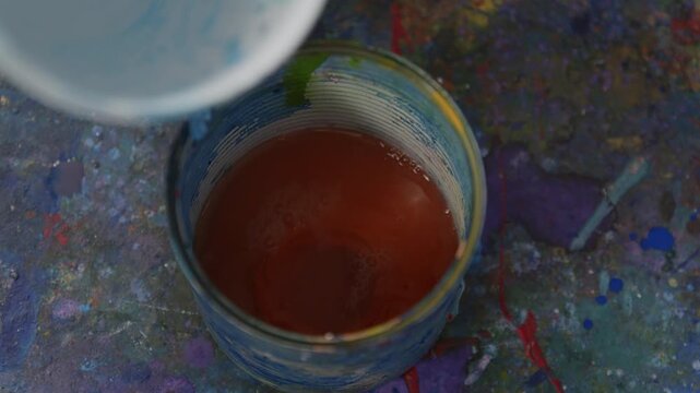 Wasser wird in orangene Acrylfarbe gegossen &ndash; k&uuml;nstlerischer Mischprozess im Studio mit Fl&uuml;ssigkeitsbewegung, Farbverd&uuml;nnung und kreativer Vorbereitung