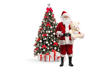 Santa Claus holding a teddy bear in front of a Christmas tree