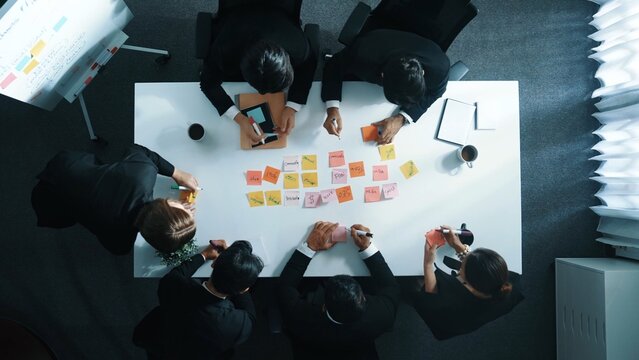 Top down aerial view of professional business people writing and sharing marketing idea on sticky note. Group of diverse executive manager working together or brainstorming strategy. Directorate. - Powered by Adobe