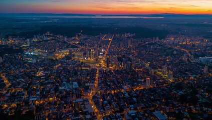 Showing urban skyline and street grid glowing at dusk, including high-rise clusters and coastline