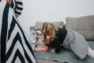 Two young children share a joyful moment playing together on a comfortable sofa. The scene radiates warmth and family harmony within a cozy home environment.