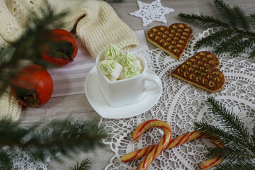 Christmas background: a mug of sweets among fir branches, cookies, and persimmons