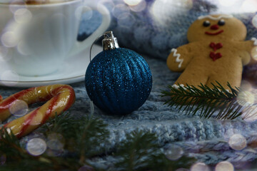 Christmas background: a blue Christmas tree ornament on a knitted piece against a backdrop of gingerbread cookies and a mug
