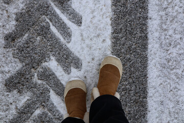 Winter travel concept: warm boots on feet on a snowy road