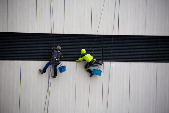 Climbers cling to safety ropes while performing dangerous work at construction site. Men wearing protective equipment in bad weather. Dangerous profession for men