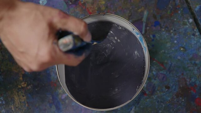 Hand r&uuml;hrt dunkle Fl&uuml;ssigfarbe im Eimer, zieht sich zur&uuml;ck und l&auml;sst einen wirbelnden Farbeffekt entstehen &ndash; kreativer Mischprozess und dynamische Studiobewegung