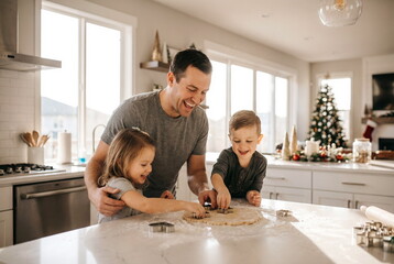 Happy father and his two children celebrating Christmas and together they bake cakes on bright modern kitchen. Family cooking education bonding concept and warm family relationships, lifestyle