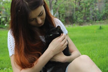 Redhead brunette girl hugging black cat on green grass