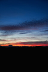 Sunset sky with layered clouds glowing in red, orange, and blue tones dark mountain silhouettes