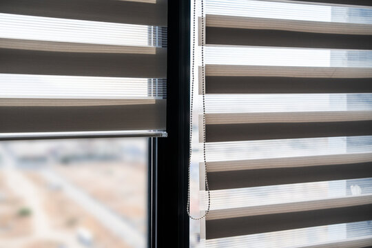 Modern zebra blinds partially open on a tall window with bright outdoor view softened by layered fabric panels