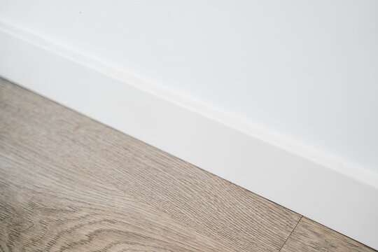 White baseboard detail with wooden textured flooring in clean minimalist interior space
