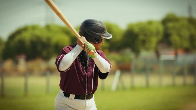 A determined baseball player in a helmet and uniform practices her powerful swing on the field. She gets into a focused batting stance, then makes an athletic, impactful swing.