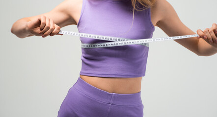 Woman measuring bust with tape in purple sportswear isolated on neutral background