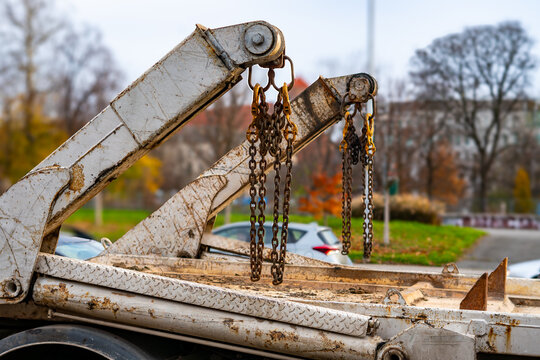 Truck loading arm with hanging chains and visible wear marks positioned on an urban parking area during daytime scene