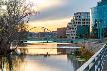 Wrocław skyline featuring Słodowa Footbridge over the Oder and modern office buildings reflecting in calm sunset water