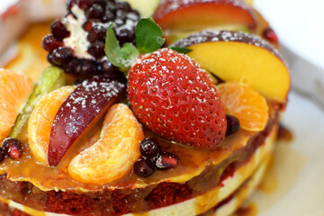 A slice of red velvet cake decorated with strawberries, pomegranate, and other fruits. Selective focus.