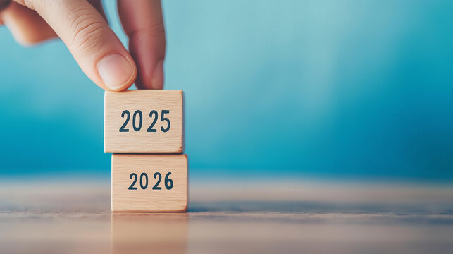 Close-up of a human hand placing a wooden block with number 6, changing year "2025" to "2026", minimalistic background, with copy space.
