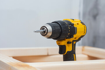 Cordless drill screwdriver stands on wooden planks during carpentry assembly work. Close-up of a...