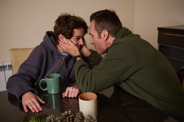 Father And Son Share Tender Moment At Table With Coffee In Home