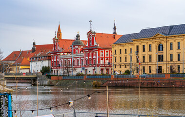 Panoramic view of Wrocław’s Ossolineum by the Oder featuring distinctive red Baroque façade reflected softly in river water